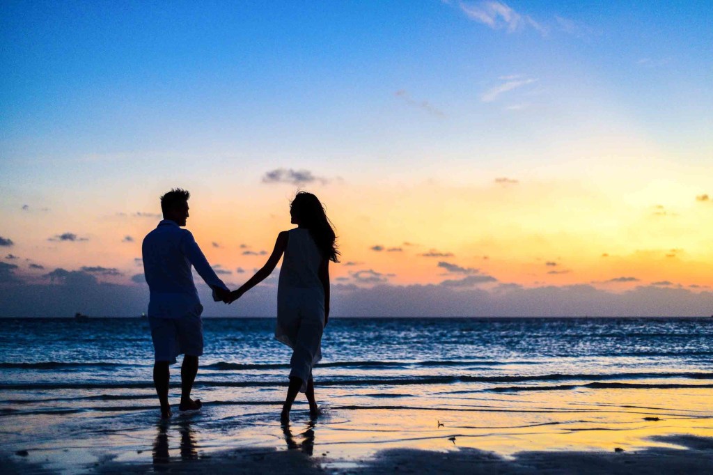 A couple holding hands on the beach at sunset