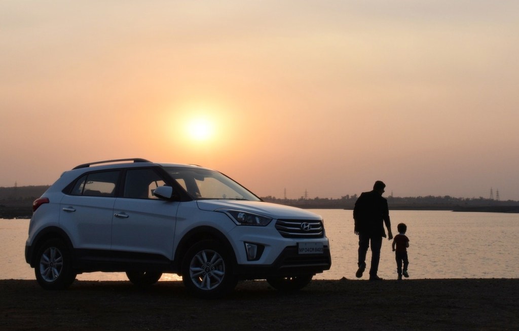 A man and a child near white SUV during sunset