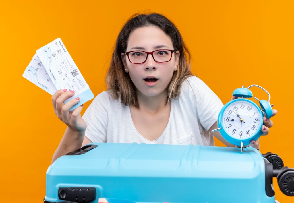 a woman holding plane tickets and a clock wondering how hard surviving long-haul flights is