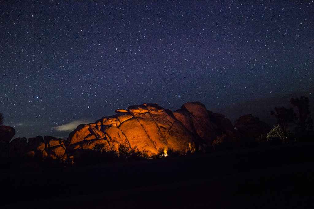 A campfire in the distance under a large rock formation