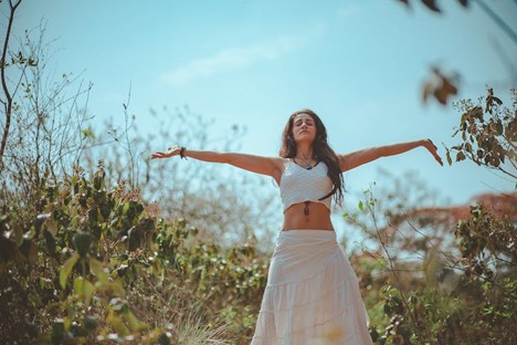Woman in a long white skirt standing outdoors and spreading her hands