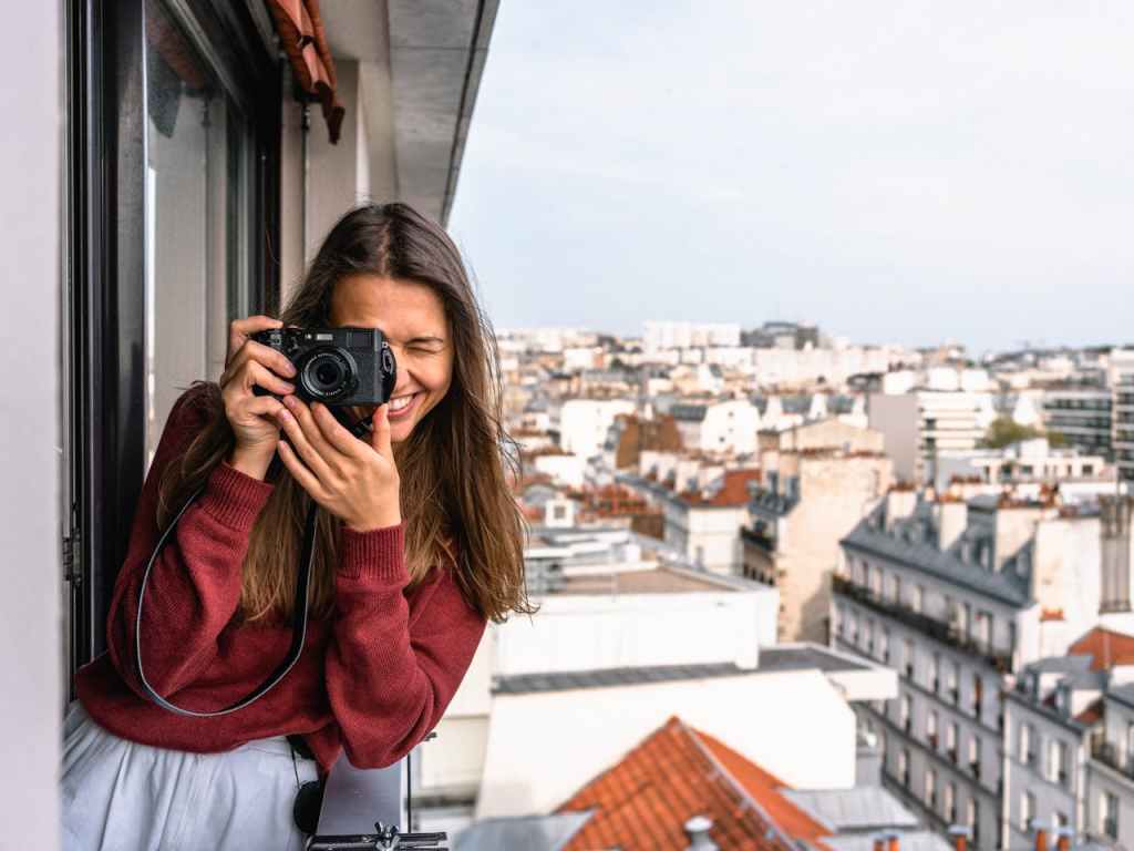 A smiling woman taking pictures on a balcony in Paris.


