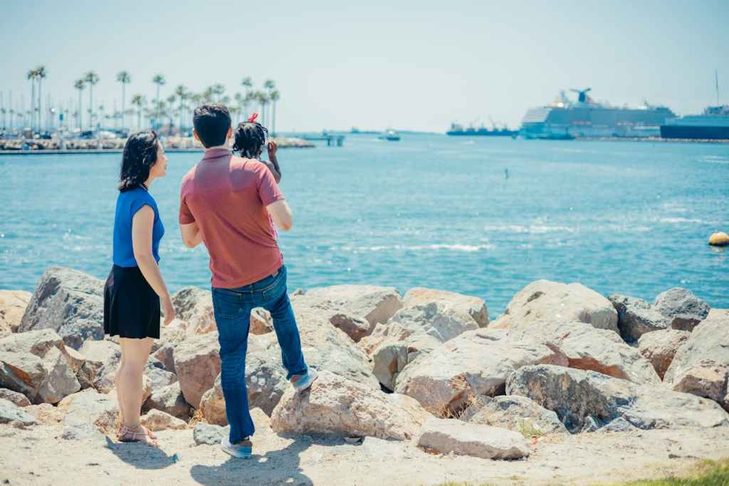 A family enjoying a scenic view of the ocean and cruise ships while standing on rocks by the shore
