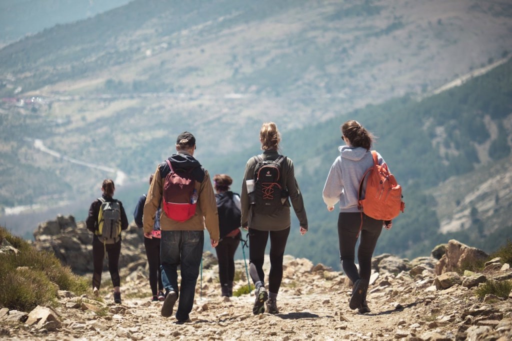 A group of hikers walking on a mountain trail, wearing backpacks and outdoor clothing, surrounded by nature