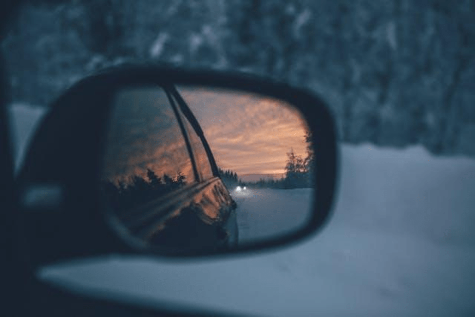 car's side mirror reflecting a snowy road at sunset
