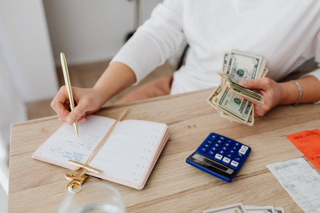 A woman holding money and writing in a notebook.